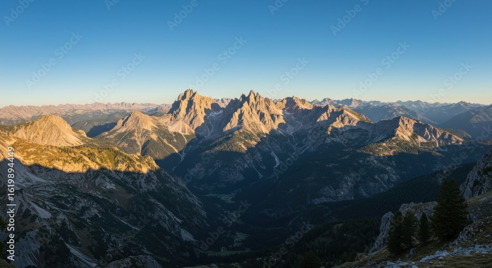Sunrise illuminates mountain peaks, casting shadows on valleys. Blue sky above, scenic alpine landscape Sunrise illuminates mountain peaks, casting shadows on valleys. Blue sky above, scenic alpine landscape