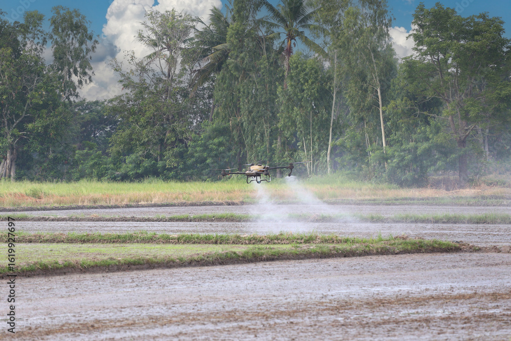 Fototapeta premium A drone effectively sprays pesticide over a farm field surrounded by lush green trees.