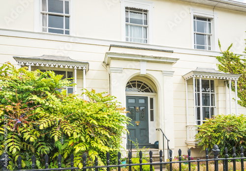 Luxury gray front door in English traditional Regency townhouse. Inviting English home entrance. Charming house with front garden and beautiful antique period features on windows.