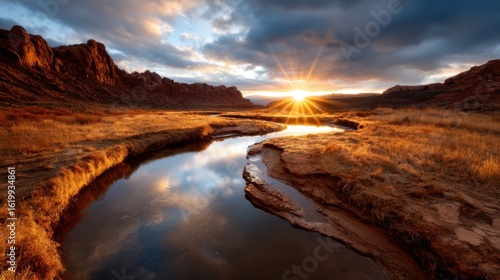 A breathtaking sunset casts warm hues over a tranquil river, framed by rocky formations and golden grass, creating a picturesque natural scene perfect for relaxation.