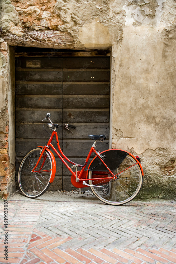 Red bicycle leaning against rustic wall with tiled pavement in old village, Tuscany, Italy, evoking slow living and rural European charm. Red bicycle leaning against rustic wall with tiled pavement in old village, Tuscany, Italy, evoking slow living and rural European charm.