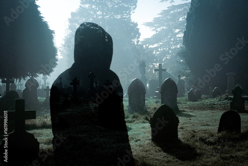 A double exposure horror edit. Of a hooded ghost like figure in a graveyard on an eerie foggy night
