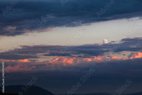 sunset over the mountains with clouds and moon