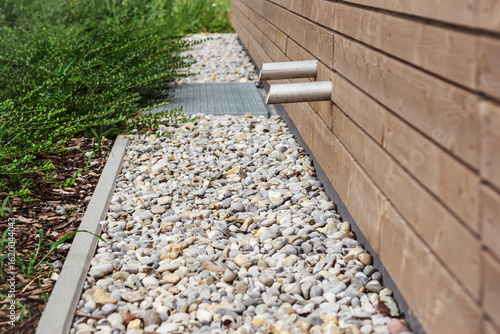 Drain Stones Gravel Rocks Draining Outdoor Floor around Building and Modern Landscaping. Franch drain along Facade Building.