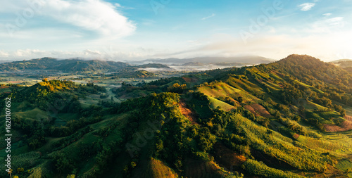 Aerial view of rolling green hills kissed by the morning sun, with wisps of fog nestled in the valleys, San Enrique, Western Visayas, Philippines.