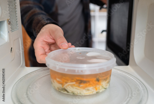 Hand placing soup container into microwave for heating.	
