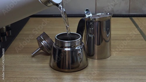 A person pours hot water into a heating vessel and assembles a moka pot