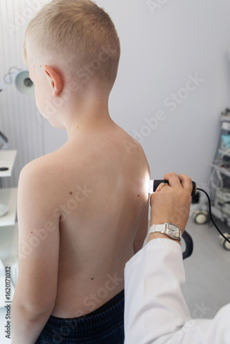A pediatric dermatologist examining a young boys skin with a dermatoscope in a medical clinic. Skin check up for moles and birthmarks.