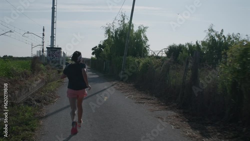 A woman exercises in a rural area next to a train tracks in the morning.