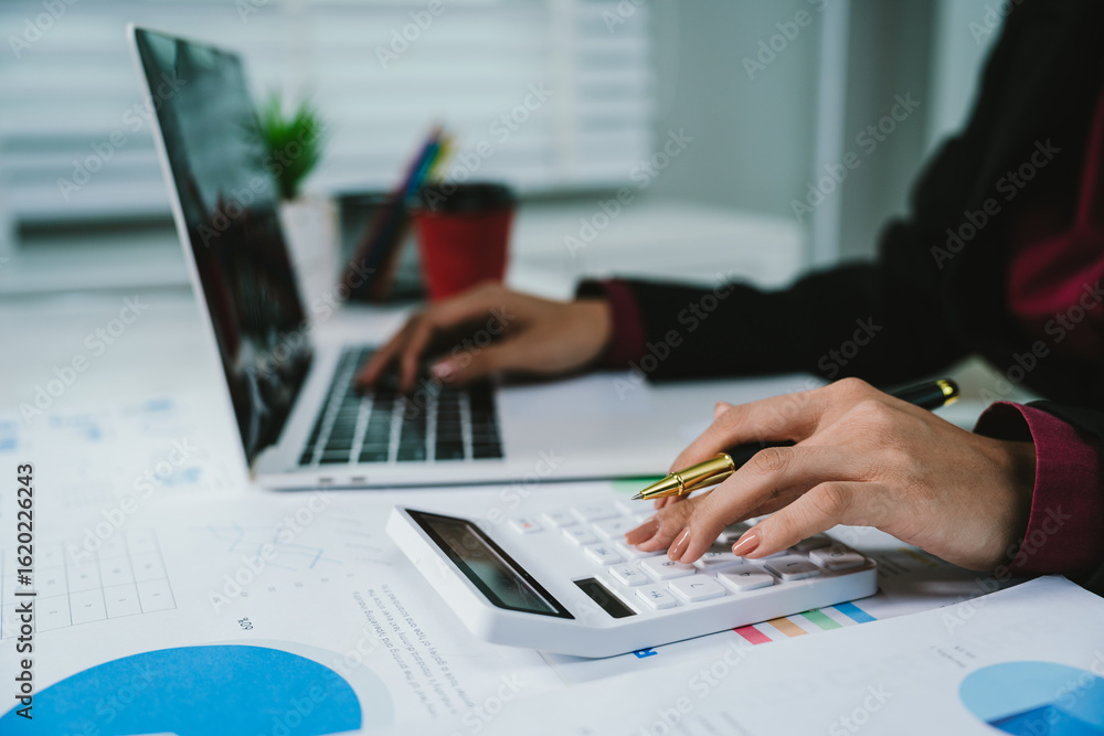 Fototapeta premium A businesswoman analyzes financial documents with charts and graphs at a desk, highlighting data trends with a pen in a bright, professional office setting.