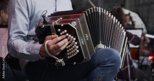 A musician playing a traditional bandoneon in an orchestra or tango ensemble. The player's hands work the buttons and stretch the bellows of the classic instrument. 