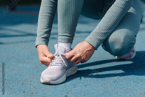 Fotografija young sportive woman lacing up shoes before doing sport exercises outdoors in su