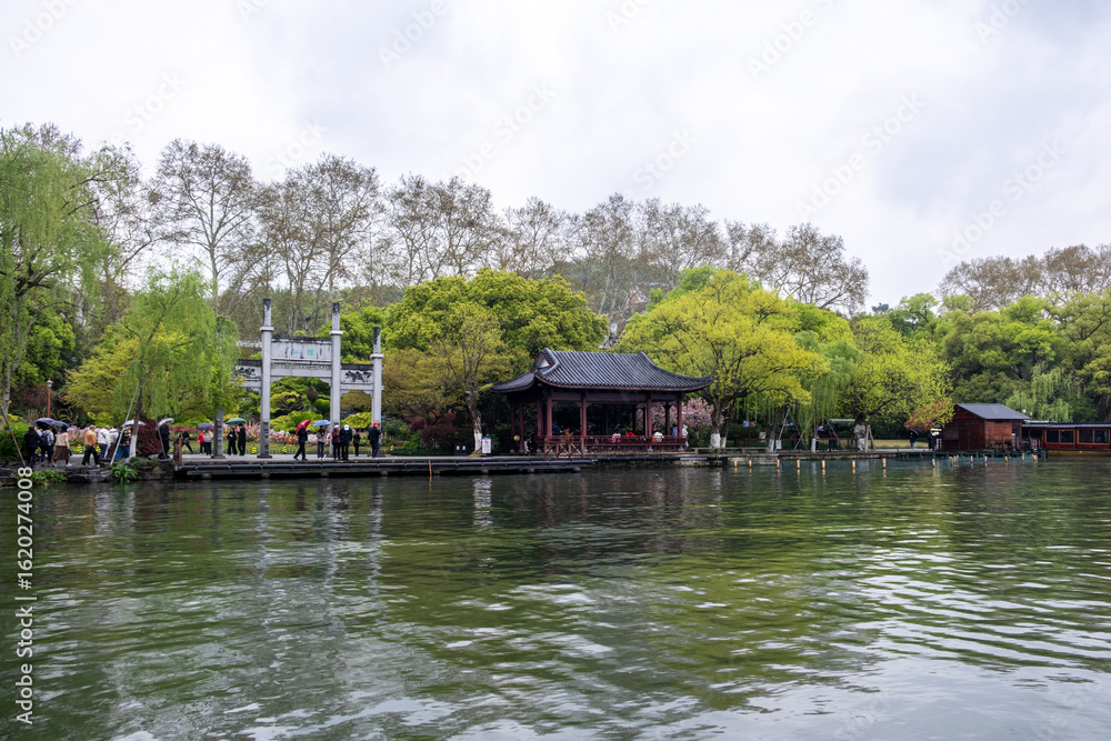 Obraz premium Hangzhou, West Lake. China. Tourists with umbrellas walk along the promenade by a traditional Chinese pavilion
