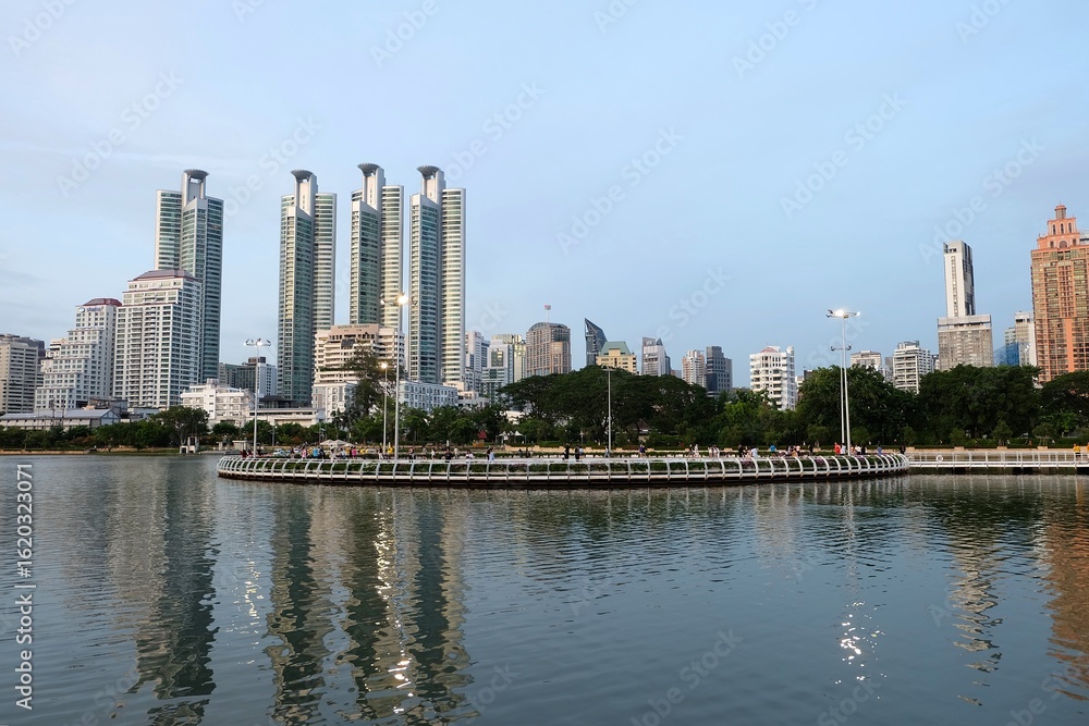 Naklejka premium A beautiful lake surrounded by a running track, with towering buildings in the background, at Benjakitti Park in Bangkok.