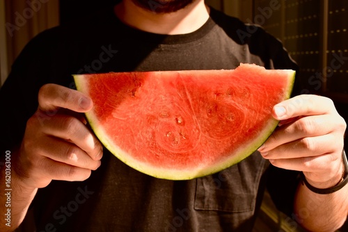 Man holding a juicy red watermelon slice. Symbol of summer, freshness, and healthy fruit rich in vitamins.