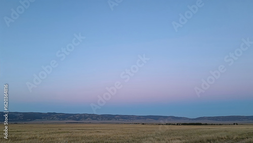 Pastoral landscape with vast field and distant mountains under a serene twilight sky creating a sense of peaceful solitude