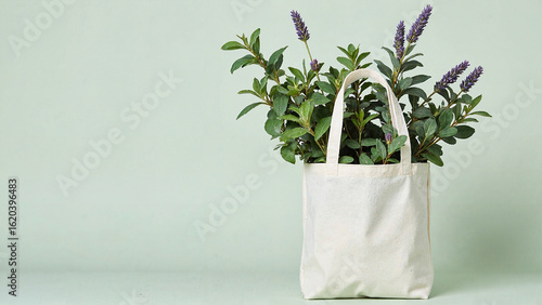 A white tote bag with green leaves and lavender in it against a light green background. Ideal for sustainable shopping and nature-related content.