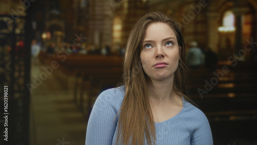 Free Download Caucasian young woman face turned sideways inside ornate church building in blue sweater; contemplation. - GFXLoad