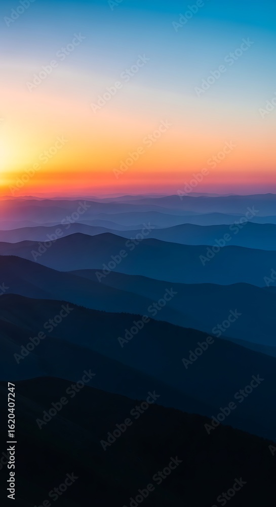Fototapeta premium Blue mountain range at sunset with orange sky and distant peaks image