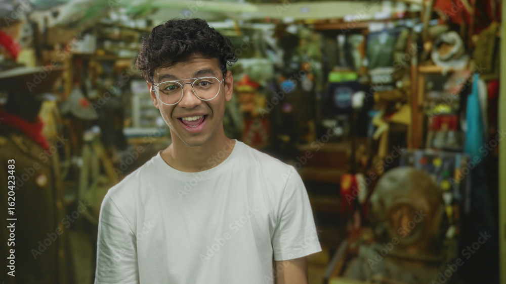 Fototapeta premium Man wearing glasses and white t shirt talking inside building hardware shop; product exploration excitement.