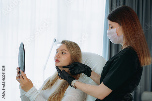woman looking in a mirror after facian rejuvenation procedure at aesthetic clinic