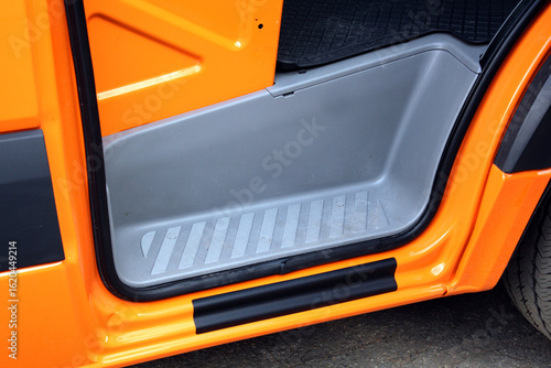 Cargo van door sill. Bright orange car door sill with gray plastic interior step and black rubber trim, showcasing durable materials and clean, modern design for vehicle entry protection.