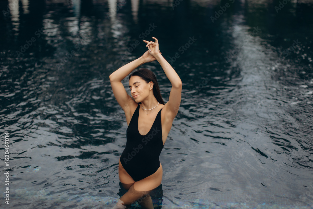 Fototapeta premium Young woman wearing black swimsuit relaxing in swimming pool