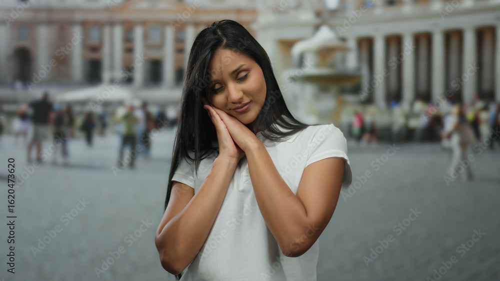Fototapeta premium Woman gesturing sleep in vatican's st. peter's square captures daytime city atmosphere, showcasing a young latina's serene expression amidst the lively outdoor setting.