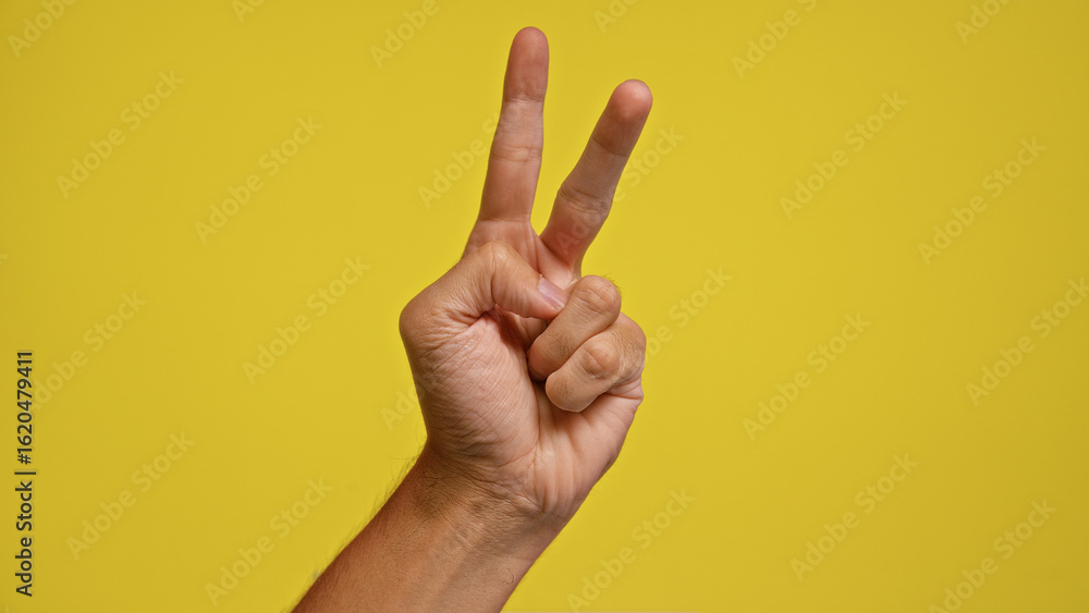 Naklejka premium Man hand showing peace gesture in front of a vibrant yellow background, emphasizing positivity and success