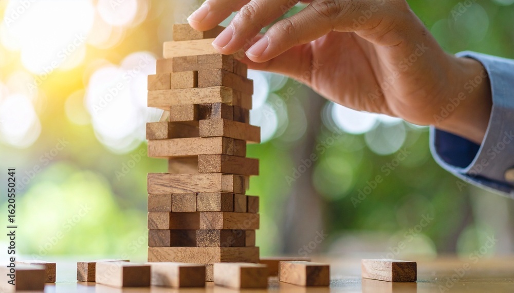Hand placing wooden block atop Jenga tower in natural light, symbolizing strategy, balance, and focus Hand placing wooden block atop Jenga tower in natural light, symbolizing strategy, balance, and focus