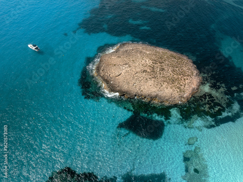 The aerial view over rock formation and a boat surrounded by crystal clear water in Formentera