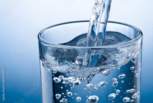 Pouring water into glass on blue background