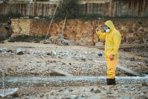 Принти на полотні Water quality inspection, Environment scientist in hazmat suit holding a water sample vial in a polluted industrial area
