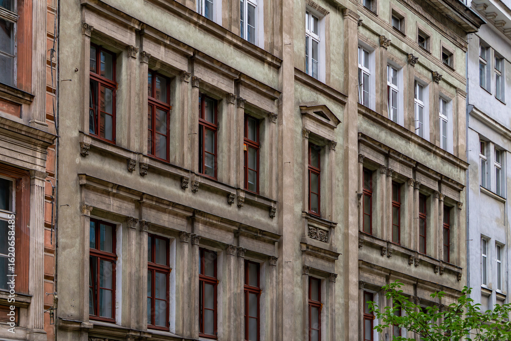 Fototapeta premium Historic tenement house in Poznań with decorative facade and red window frames, 19th-century urban architecture.