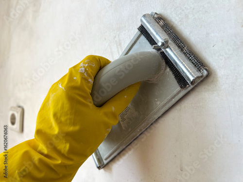Construction worker sanding wall with hand sander during home renovation