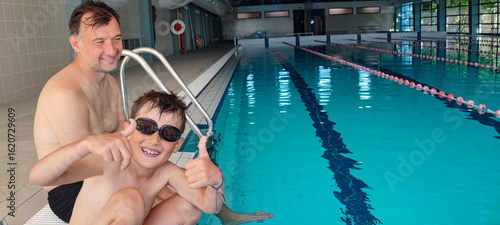 Fotografija A father helps his son with swimming goggles in a large indoor pool