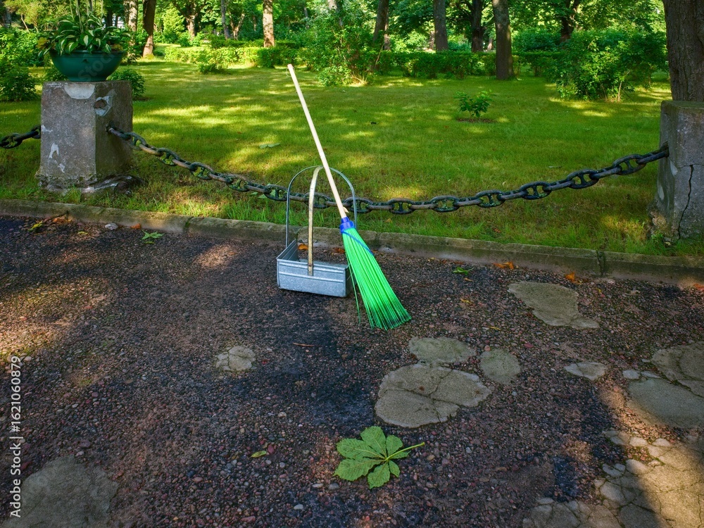 Fototapeta premium Broom and Dustpan in Park on a Sunny Day. Ideal for concepts related to public space maintenance, cleanliness, or gardening.