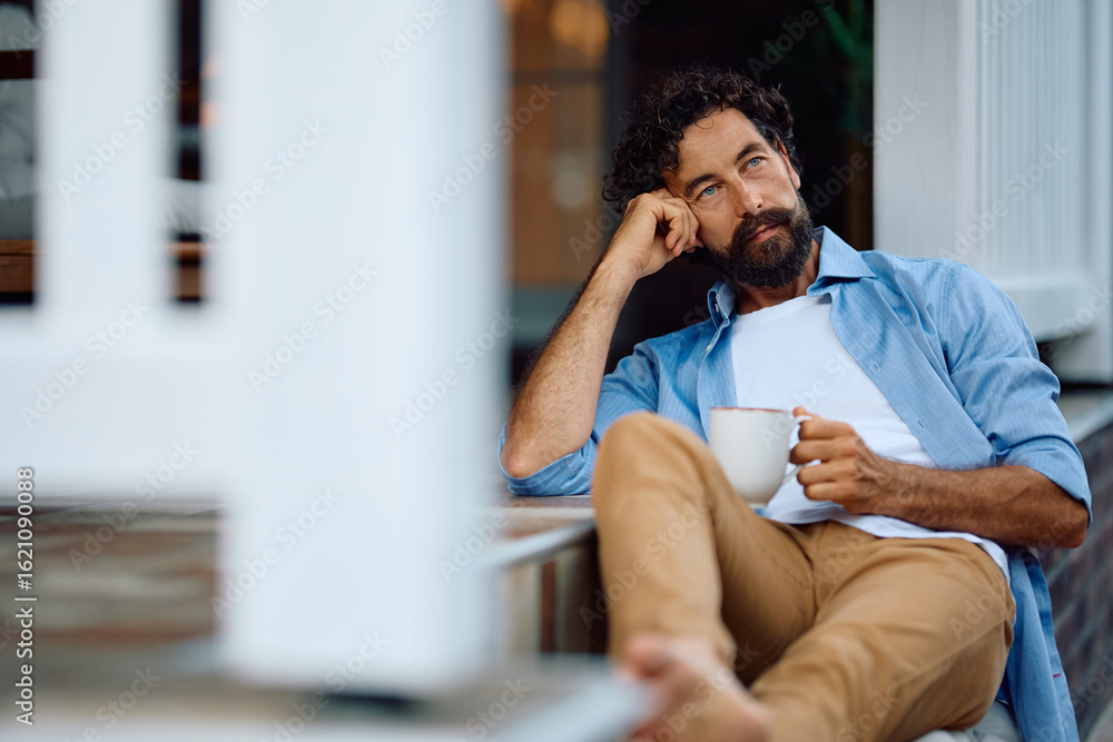 Fototapeta premium Pensive man having cup of coffee while relaxing on patio at home.