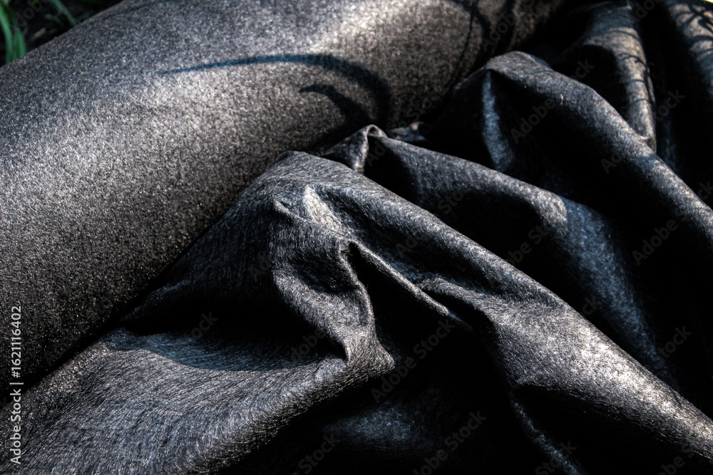 Obraz premium closeup of a thick roll of black landscape fabric partially rolled out for installation. landscaping or construction design element or banner.