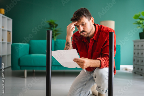 Obraz na plátně Confused man reading instructions for assembling furniture at home