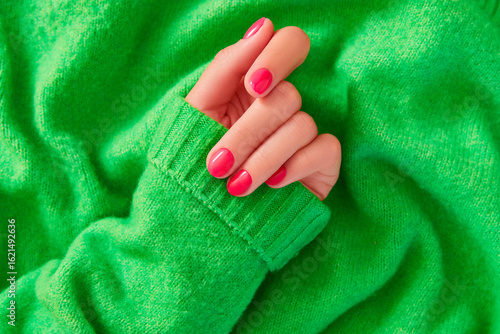 Beautiful womans hand with autumn winter pink nail design on green background. Manicure, pedicure beauty salon concept