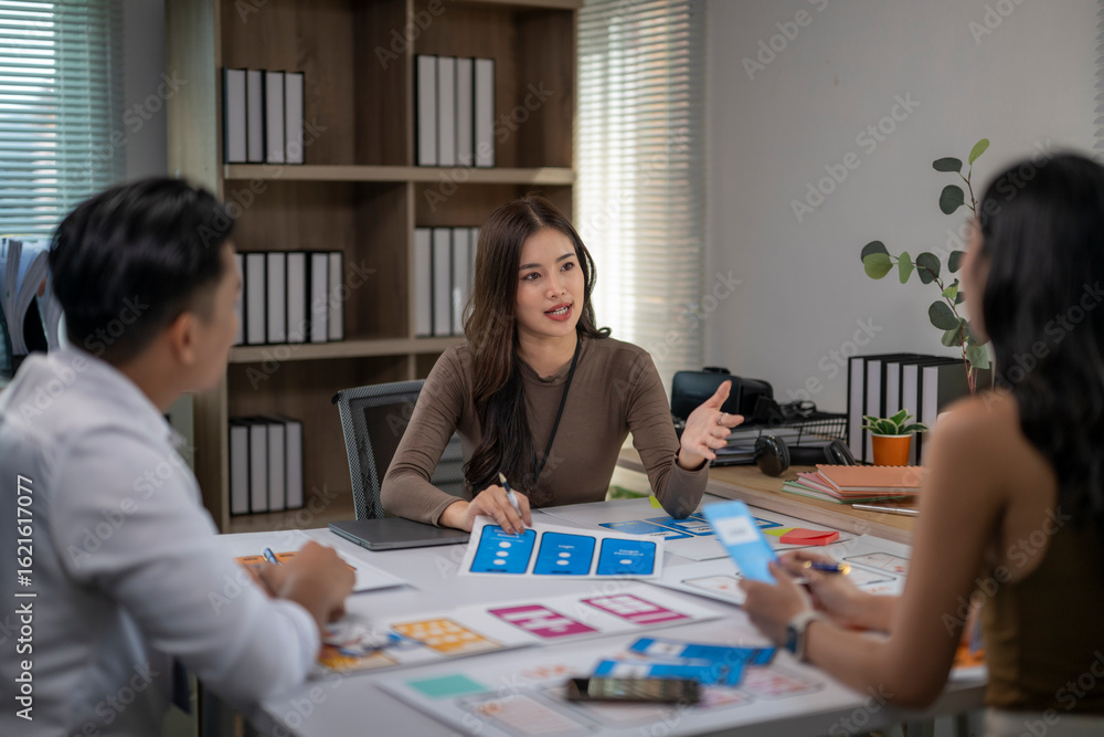 Fototapeta premium Three people are sitting at a table with papers and a laptop