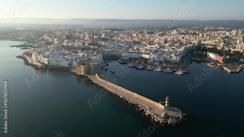 Wallpaper Mural Coastal Cityscape: An aerial view captures a coastal cityscape, where a stone pier stretches out into the tranquil sea, guiding toward a distant lighthouse. Monopoli, Puglia Torontodigital.ca