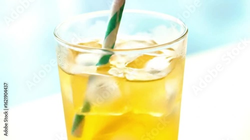 A tall glass filled with a lemonade, ice cubes and a striped straw against a bright background