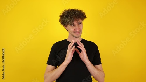 Scheming man with a wicked grin rubs his hands together against a yellow studio backdrop. Ideal for Halloween promos, villain-themed campaigns, and dark humor content.