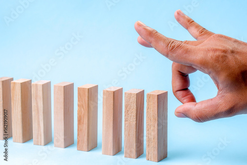 A Hand Prepares To Flick The First Wooden Block In A Domino Chain On A Blue Background