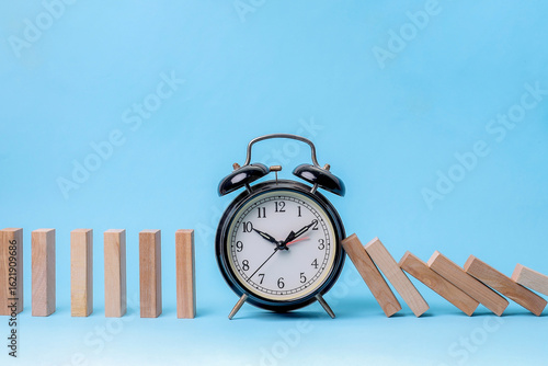 Black Alarm Clock Blocks Falling Dominoes, Symbolizing Timing Interruption