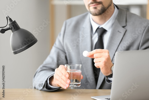 Young businessman with soluble tablet and glass of water in office, closeup