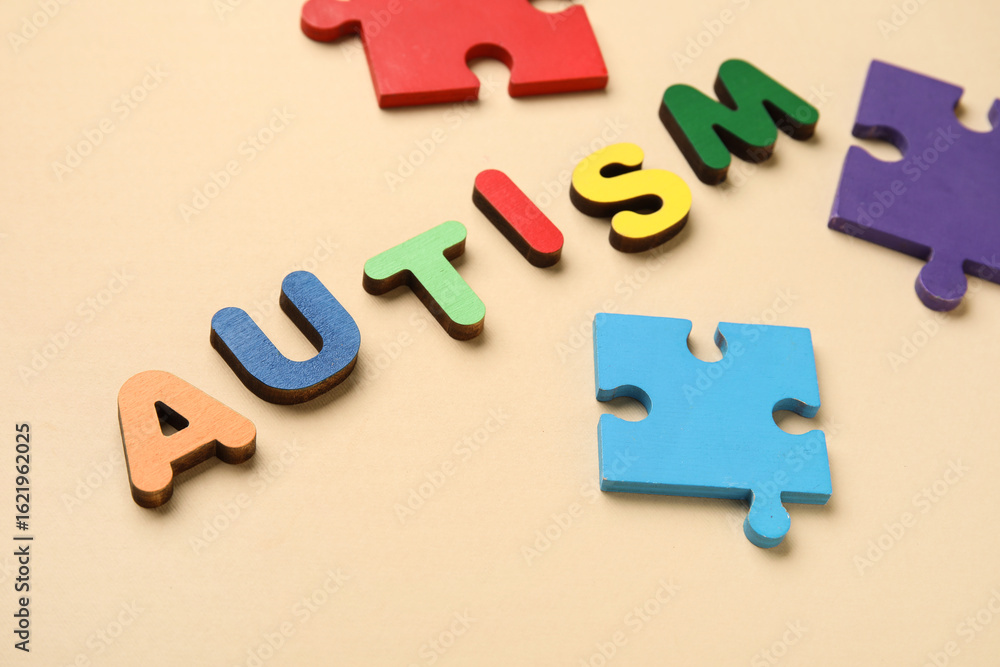 Obraz premium Word AUTISM and colorful puzzle pieces on beige background