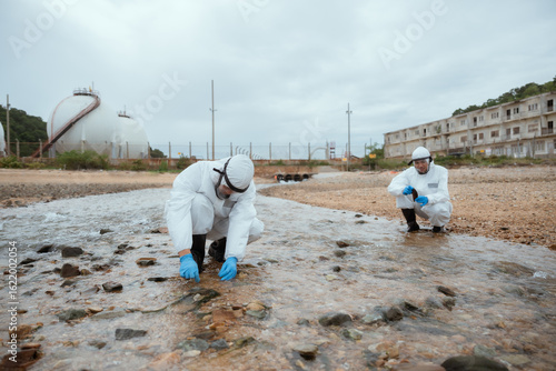 Two men in protective gear collect water samples from forest stream. Environmental scientists perform water quality testing, monitoring fresh water. Researchers conduct wetland studies.